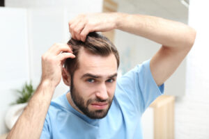 Young man indoors examining hair thinning, considering Alma TED treatments for non-invasive hair restoration and scalp rejuvenation.