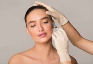 Young woman receiving a Botox injection for wrinkle reduction, illustrating plastic surgery and beauty treatment concepts, isolated against a studio wall background