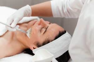 Woman receiving rejuvenating anti-aging facial chemical peel with retinol mask at beauty salon, concept of skincare and wellness treatment.